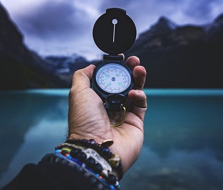Hand holding a compass in front of a lake.
