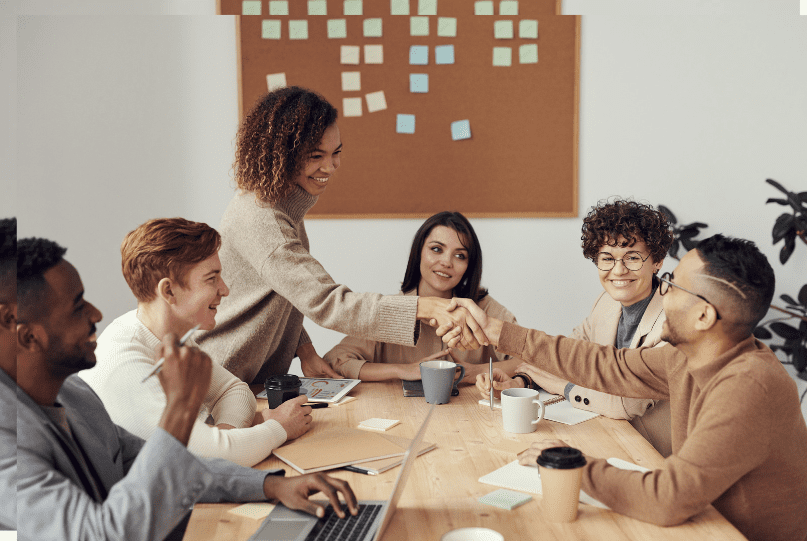 A group of people sitting around a table shaking hands.