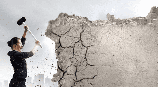 Woman breaking through stone wall with sledgehammer.