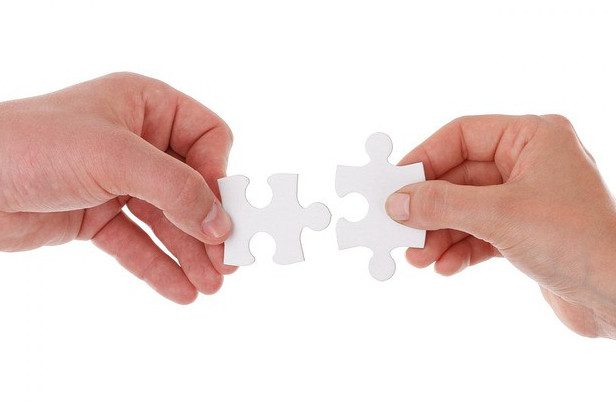 Two hands holding puzzle pieces to make a connection.